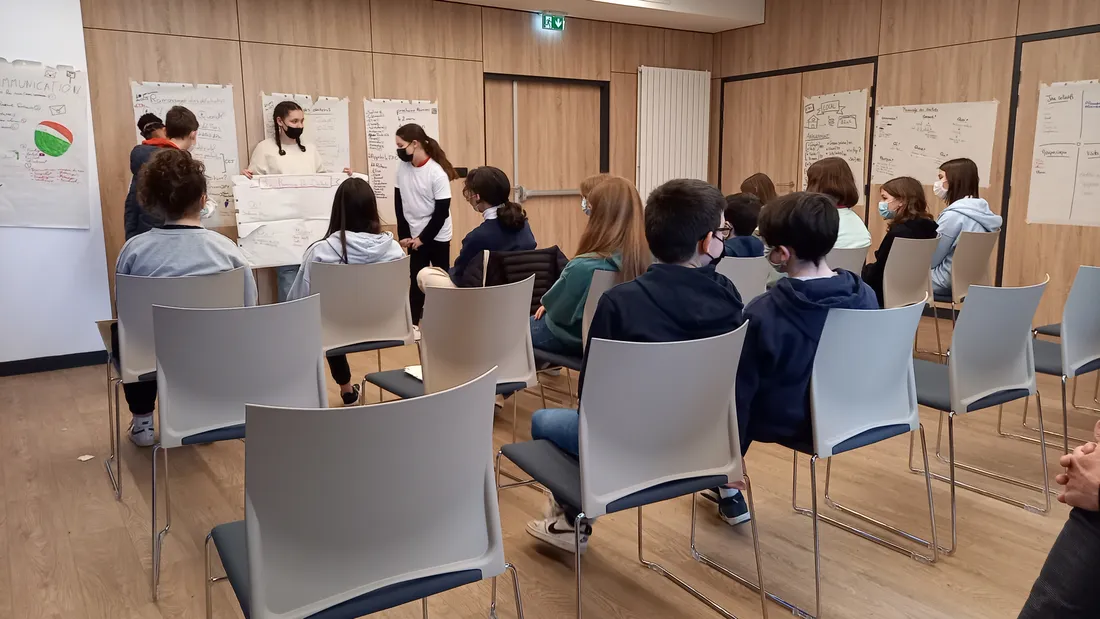 Les groupes présentent à l'assemblée leur travail, affiche à la main. 