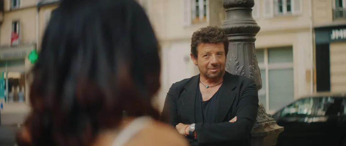 Patrick Bruel se tient debout, appuyé contre un réverbère