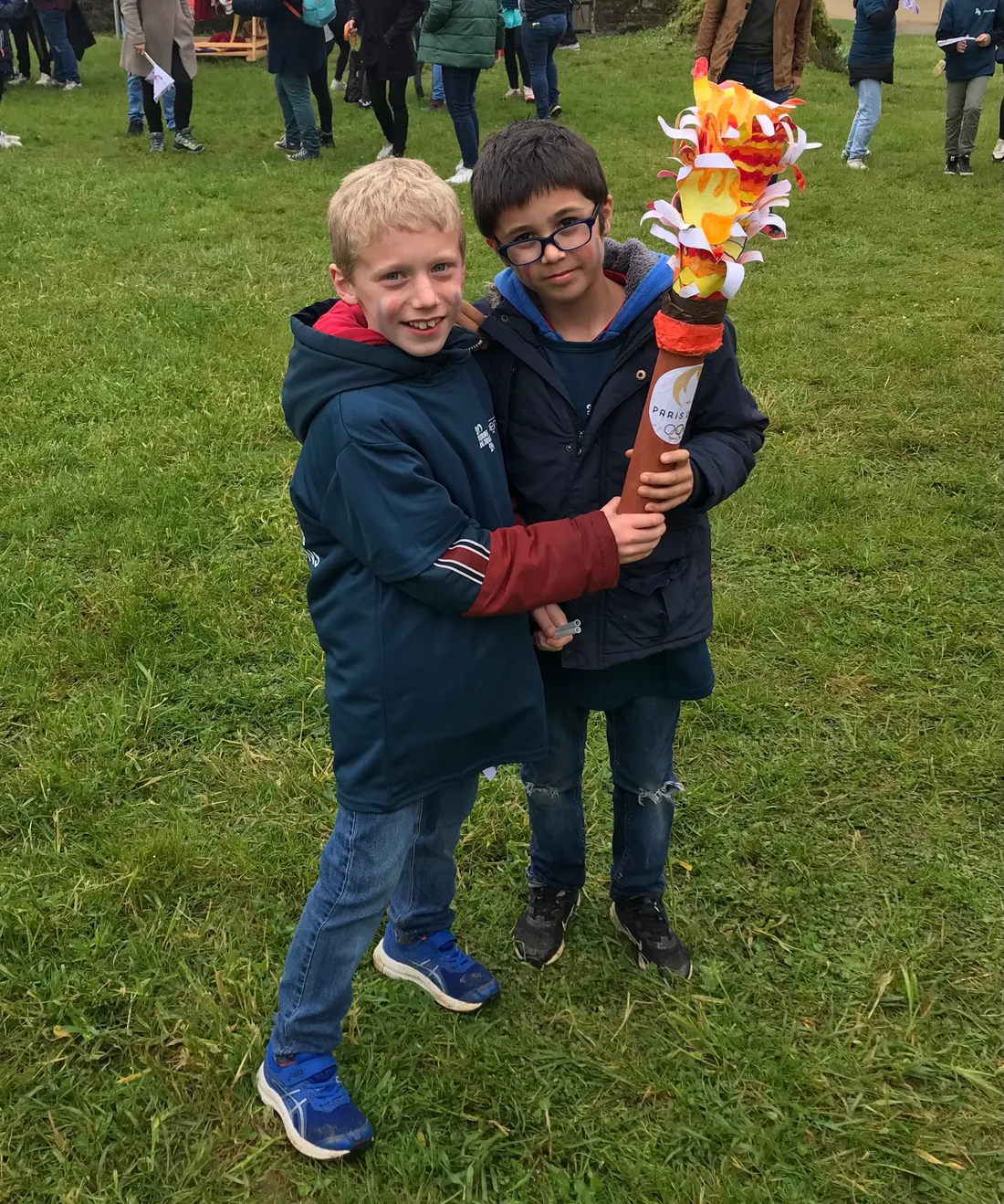 Les deux jeunes hommes montrent fièrement leur Flamme olympique reproduite. 