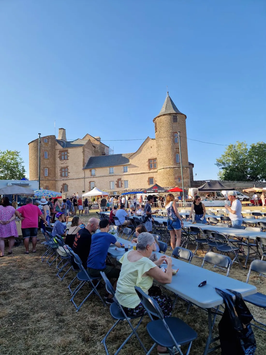 Marché gourmand avec visiteurs et stands devant le château d’Onet Village (Aveyron).